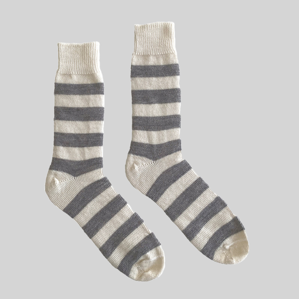 A pair of crew socks with horizontal stripes in dark gray and cream, displayed against a solid light gray background.