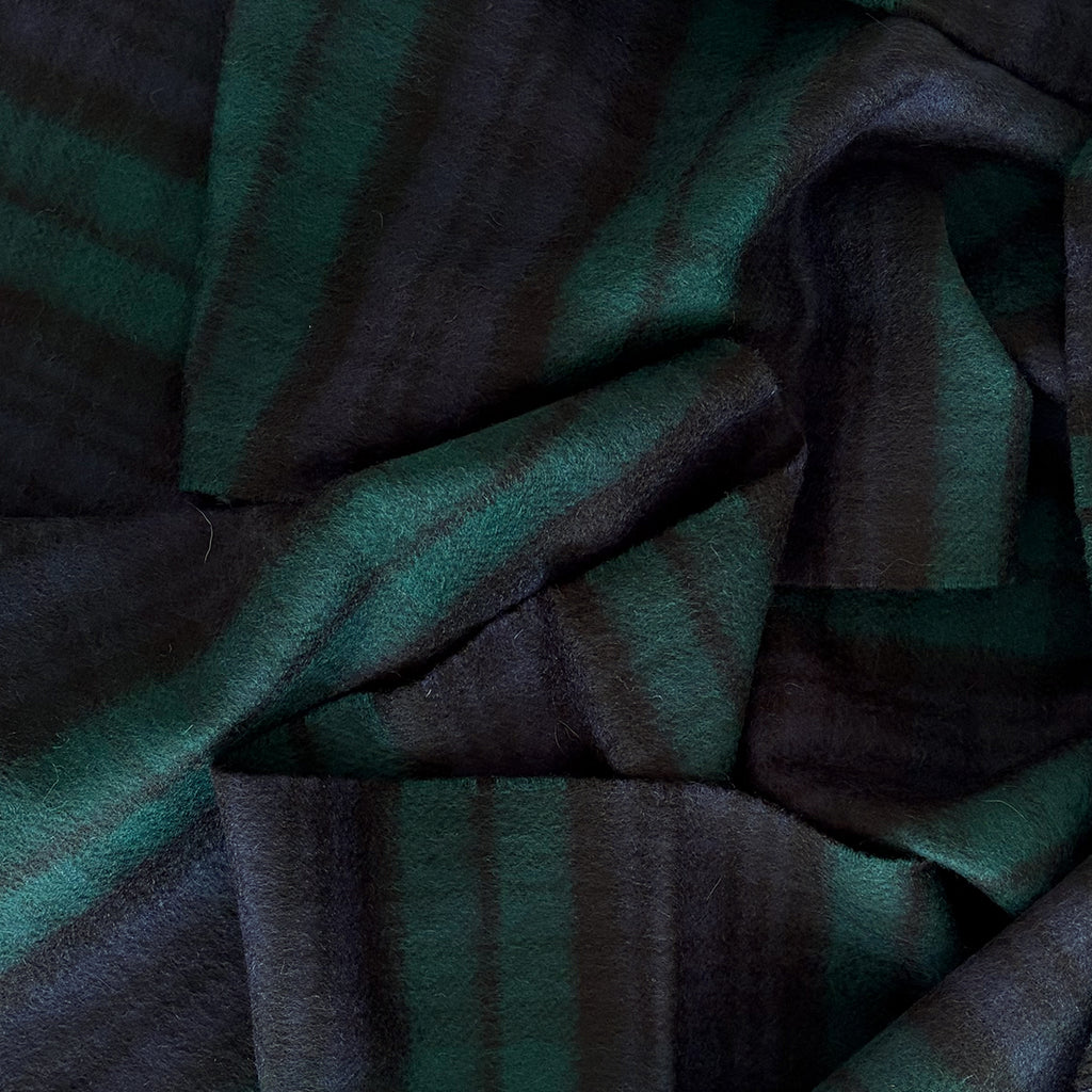 A close-up of a cashmere scarf with a dark green and navy blue tartan, showing the soft texture and folds of the material.