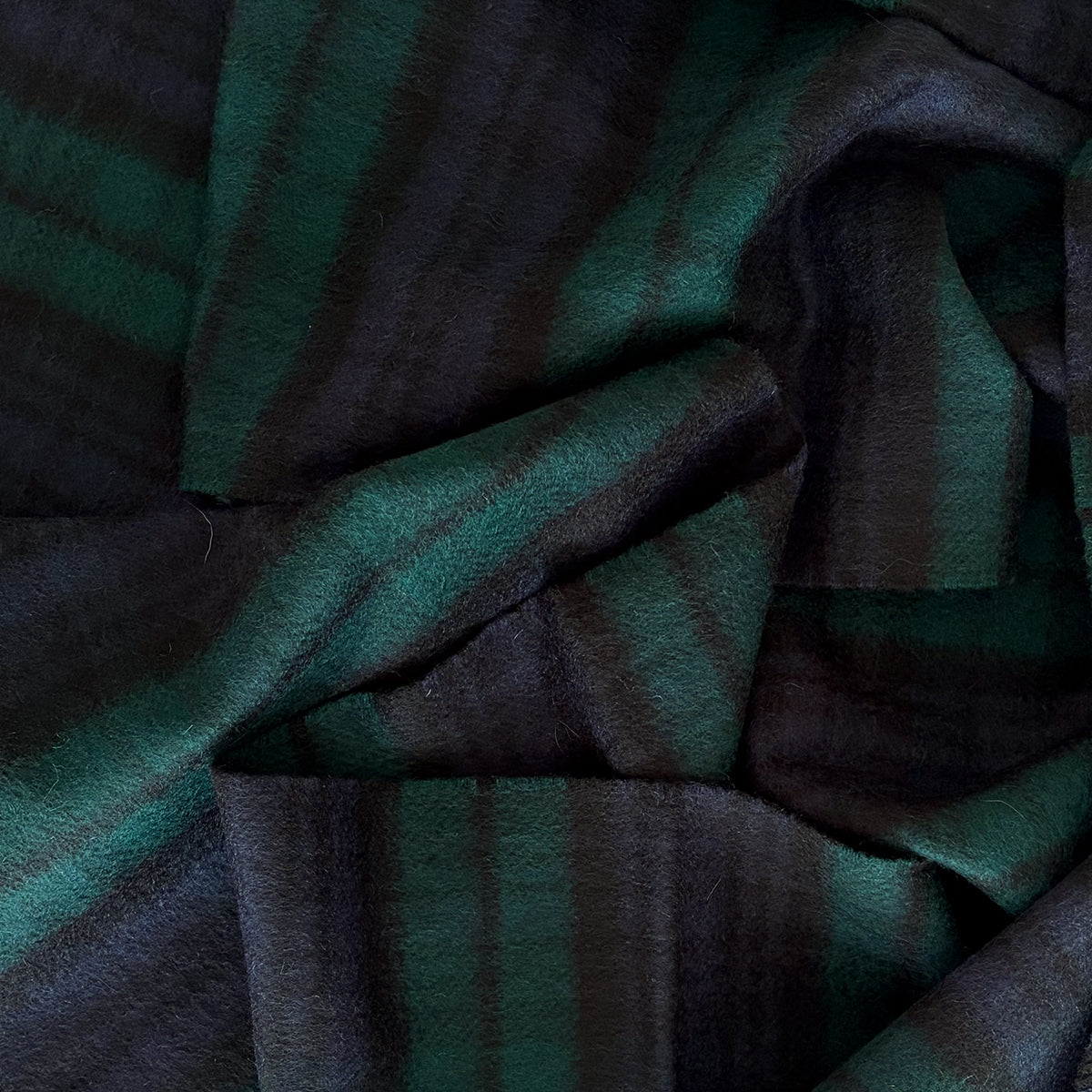 A close-up of a cashmere scarf with a dark green and navy blue tartan, showing the soft texture and folds of the material.