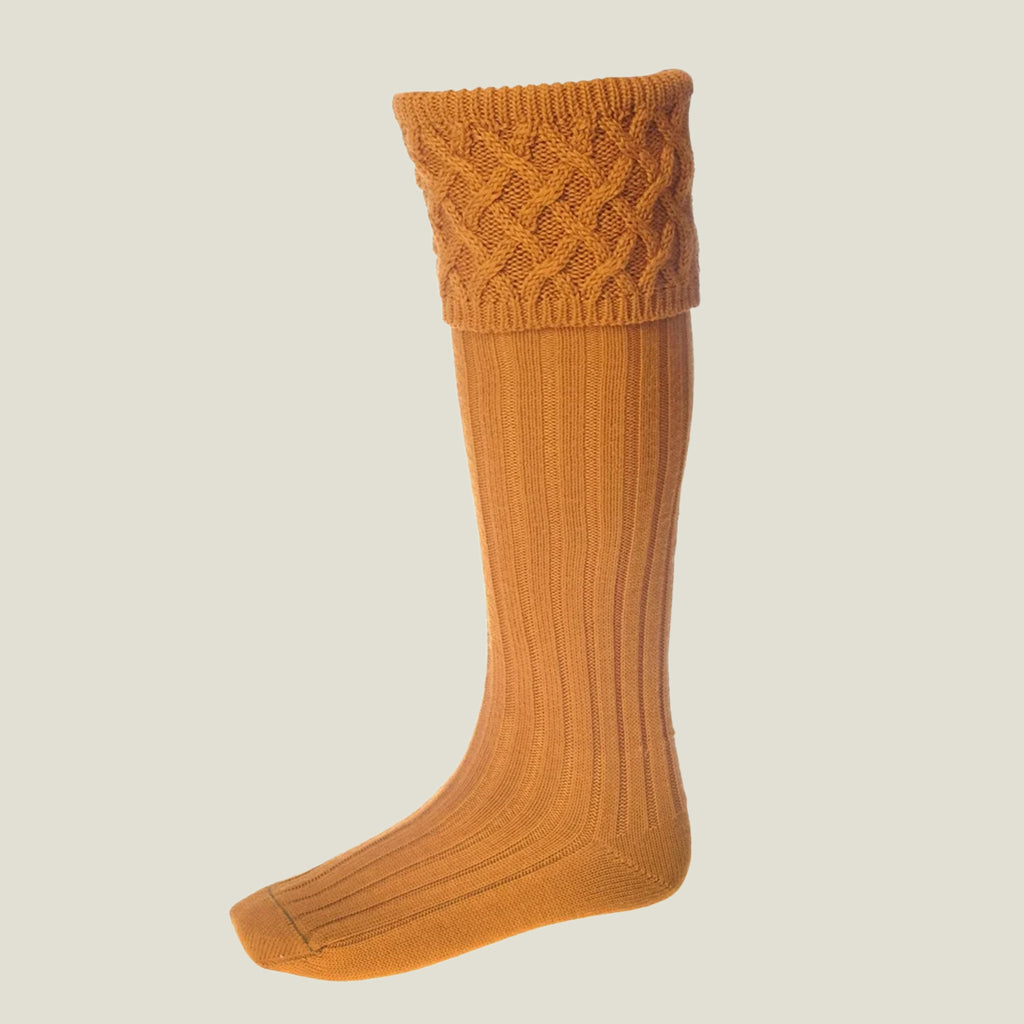 A single knee-high ribbed knit sock in a warm yellow orange ochre colour, featuring a textured cable-knit cuff, shown against a solid light gray background.