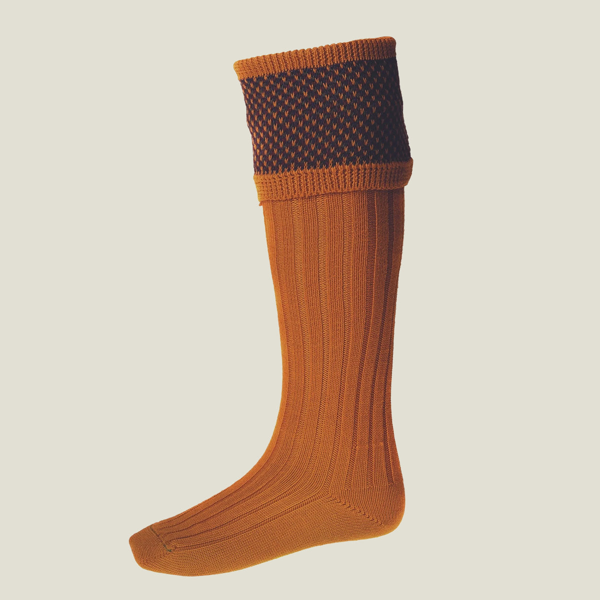 A merino blend ribbed knee-high sock in ochre orange/yellow, featuring a patterned edge in a birdseye design.