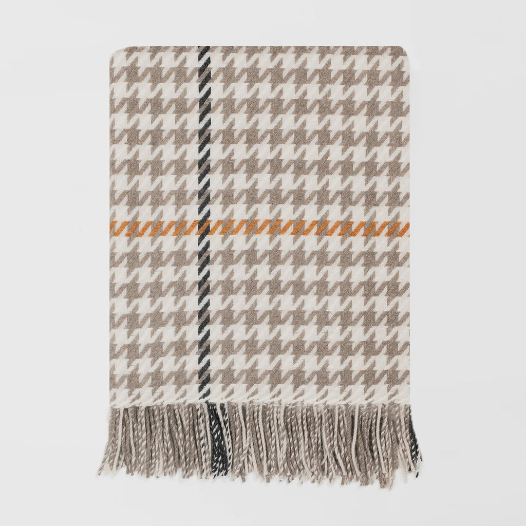 A woven throw blanket with a beige and white houndstooth pattern, featuring a central vertical stripe in black and beige, a horizontal orange stripe, and fringed edges at the bottom, shown against a light grey background.