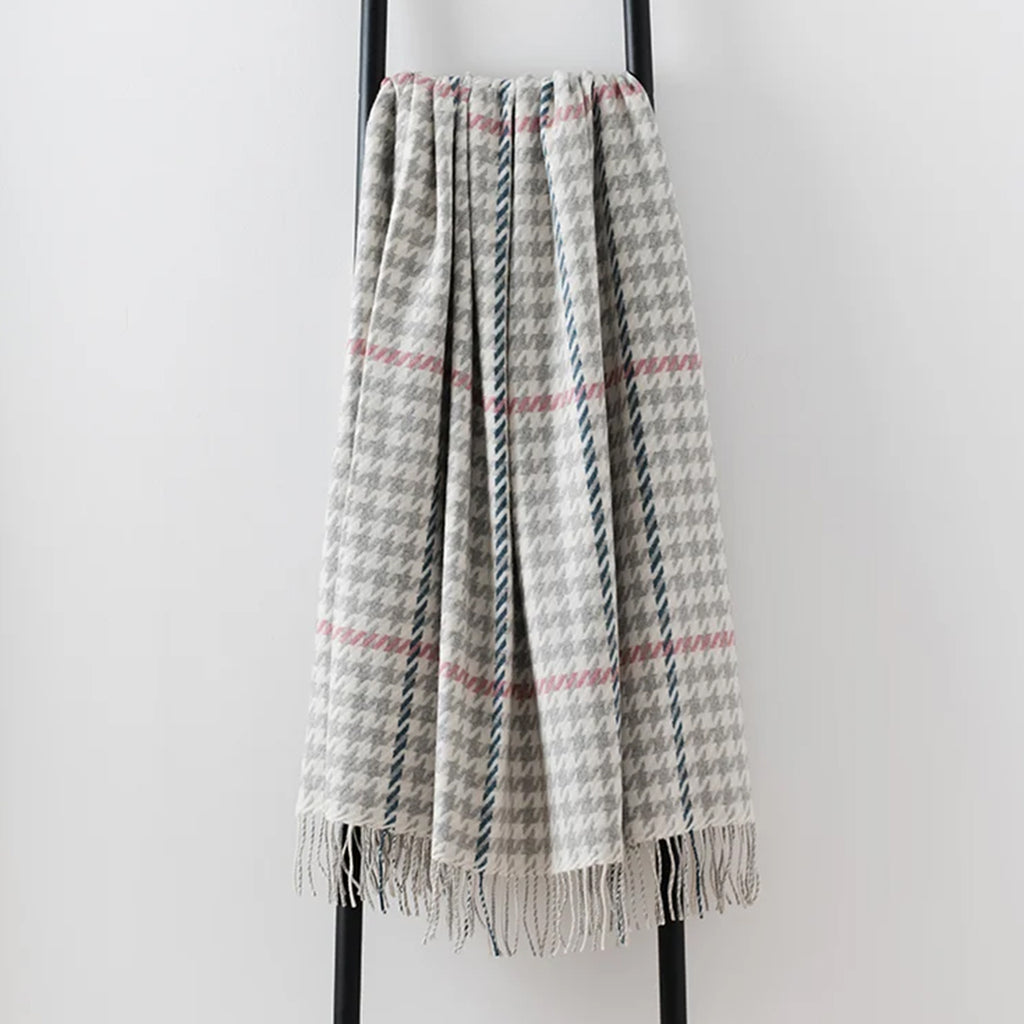 A woven lambswool throw blanket with a gray and white houndstooth pattern, accented by pink overcheck, draped over a black metal stand against a light gray background.