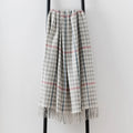 A woven lambswool throw blanket with a gray and white houndstooth pattern, accented by pink overcheck, draped over a black metal stand against a light gray background.