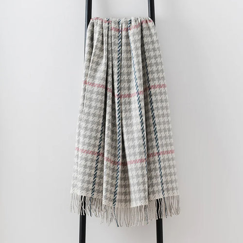 A woven lambswool throw blanket with a gray and white houndstooth pattern, accented by pink overcheck, draped over a black metal stand against a light gray background.