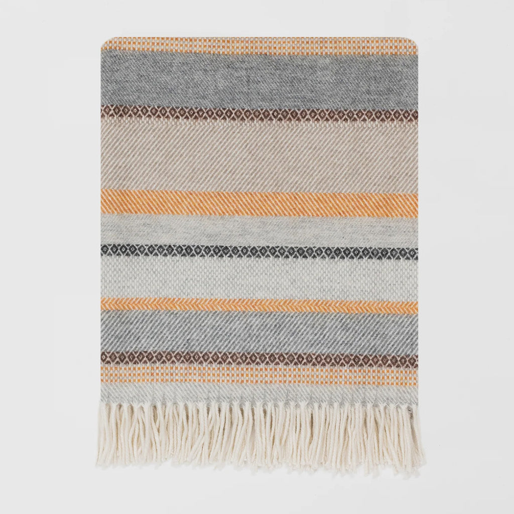 A woven lambswool throw blanket with horizontal stripes in grey, beige, orange and brown, finished with a cream-coloured fringed edge, shown against a plain light grey background.