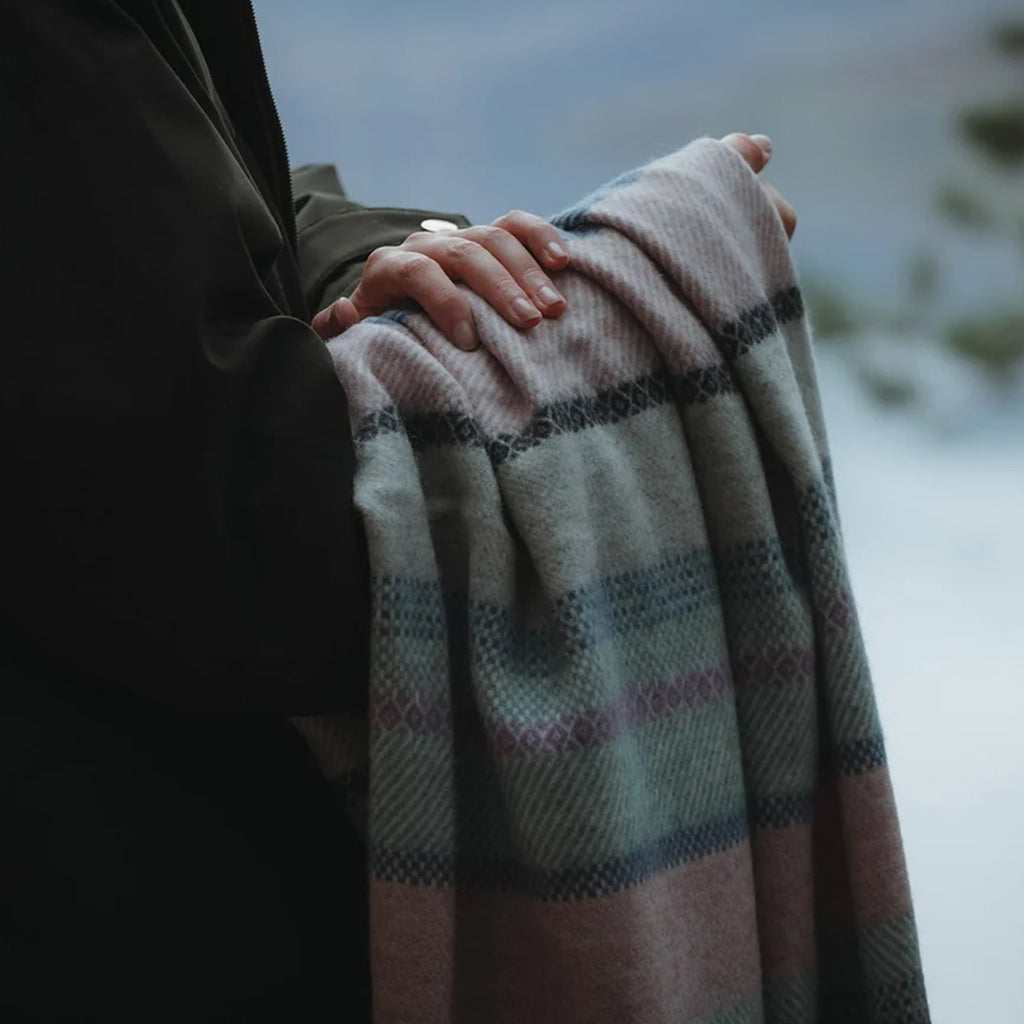 A close up of a fair isle lambswool Remony throw draped over a woman's arm.