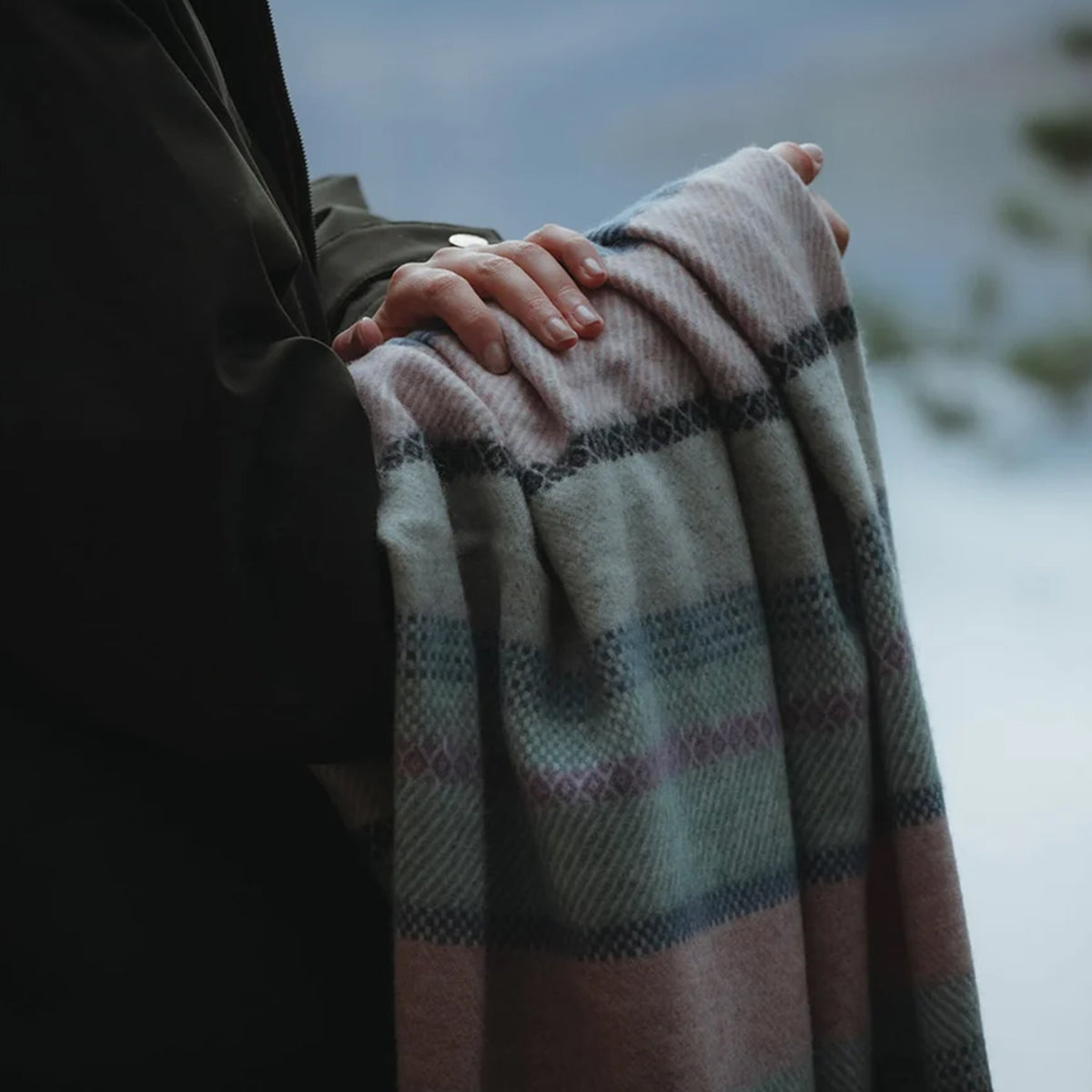 A close up of a fair isle lambswool Remony throw draped over a woman's arm.