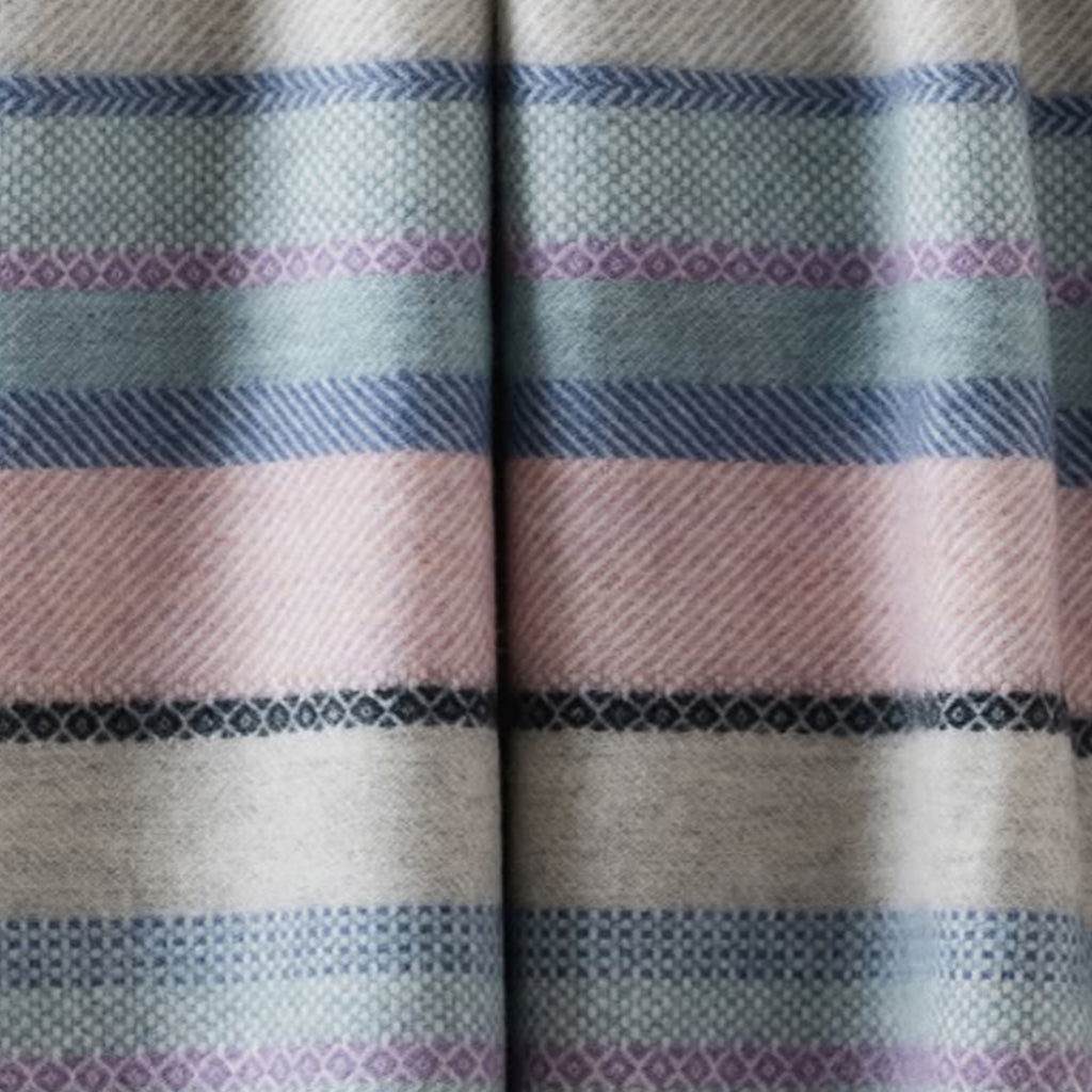 A close-up of a striped woven blanket with horizontal dusty pink, light blue, purple, beige, and black stripes with a fair isle pattern.