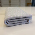 A folded knit blanket with a light grey and pale lilac wavy pattern, resting on a white countertop in a kitchen setting.