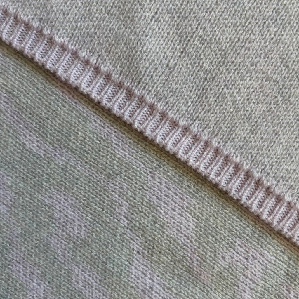 A close up of the two sides of a cashmere wrap - one side in solid pale grey and the other features a detailed grey and lilac bird's eye jacquard knit design.