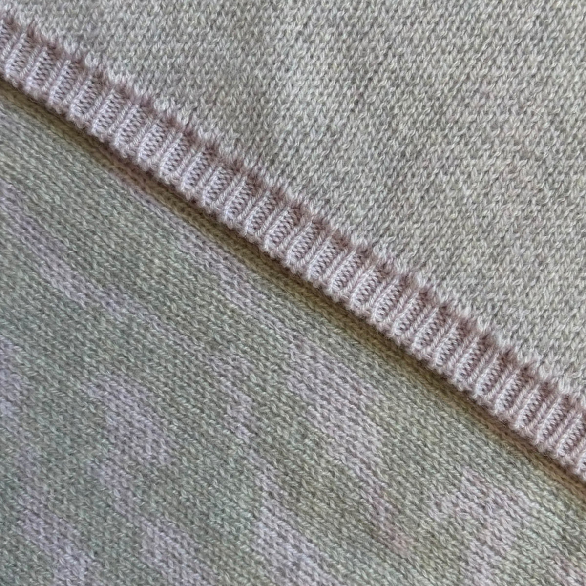 A close up of the two sides of a cashmere wrap - one side in solid pale grey and the other features a detailed grey and lilac bird's eye jacquard knit design.