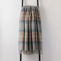 A recycled wool throw draped over a black metal stand - in a pale blue, beige and coral pink shade with an elegant fringe edge.
