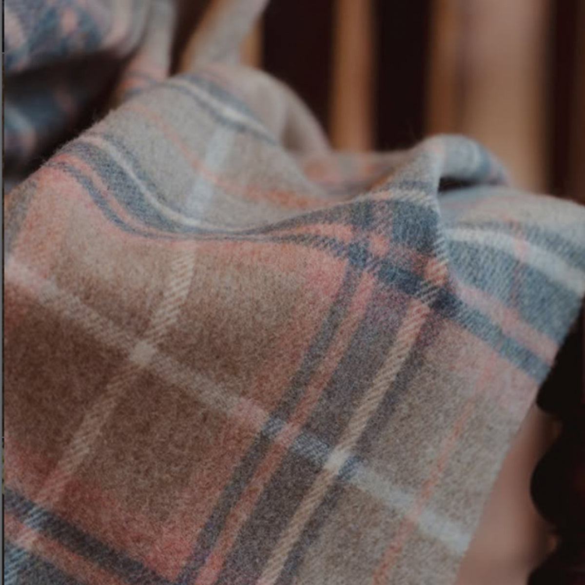 A close-up of a soft plaid fabric with a warm beige base, intersecting lines in dusty blue, muted pink, and off-white.