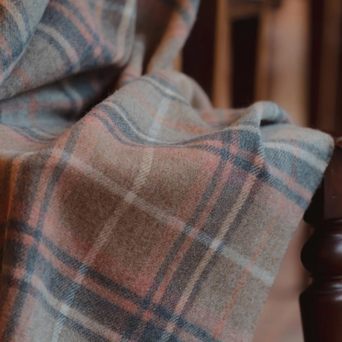 A close-up of a soft plaid fabric with a warm beige base, intersecting lines in dusty blue, muted pink, and off-white.