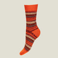 A single crew merino wool sock with a vibrant boom orange base and a detailed multicolor Fair Isle pattern in dark brown and cream, shown against a solid light gray background.