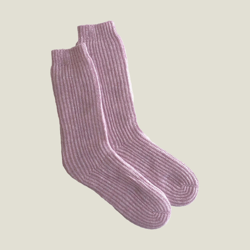 A pair of ribbed knit ribbed cashmere socks in a dusty mauve-pink color, displayed against a solid light beige background.