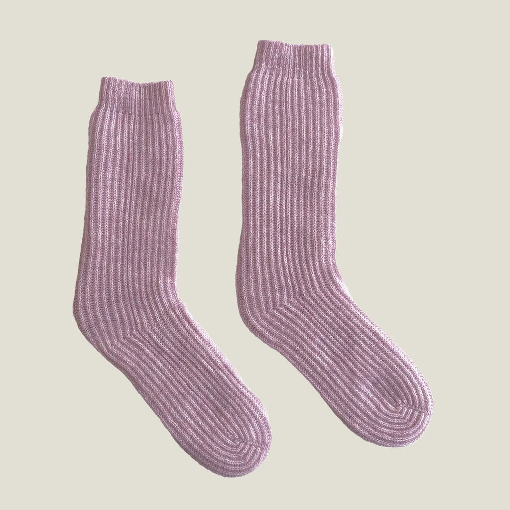 A pair of ribbed knit cashmere socks in a lilac pink color, displayed against a solid light beige background.