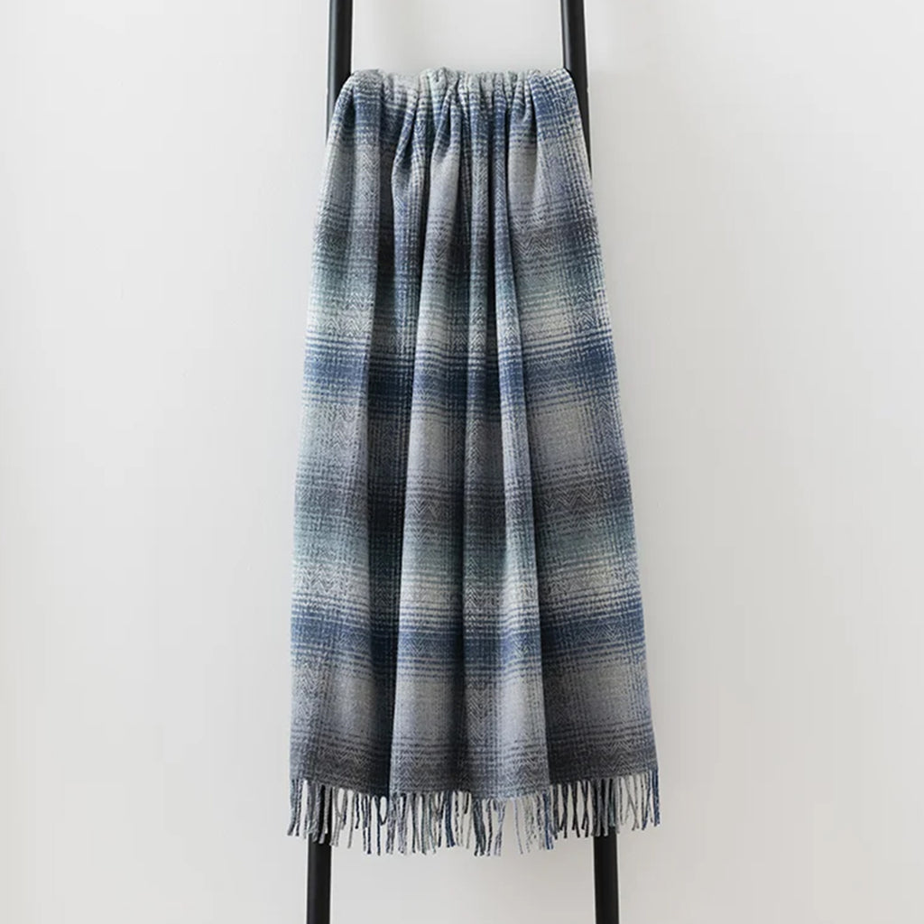 A fringed throw blanket with a blue, gray, and white striped pattern, draped over a black metal stand against a plain white wall.