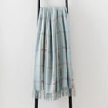 A 100% merino lambswool Remony throw draped over a black metal stand - in a pale blue shade with an elegant fringe edge.