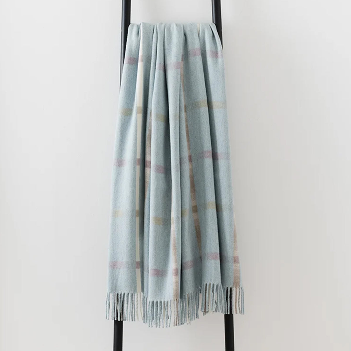 A 100% merino lambswool Remony throw draped over a black metal stand - in a pale blue shade with an elegant fringe edge.