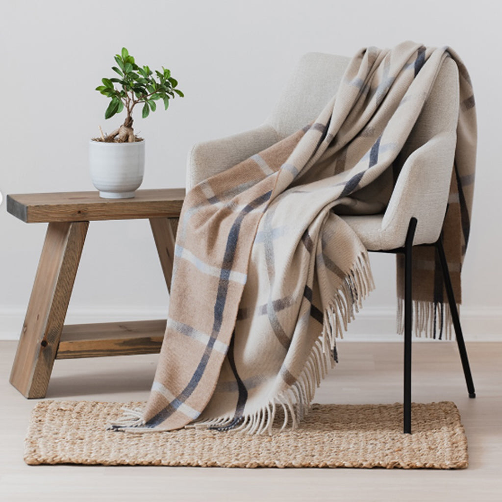 An oversized Remony merino blanket with a subtle reversible design draped over a chair with a bench behind and small rug underneath.