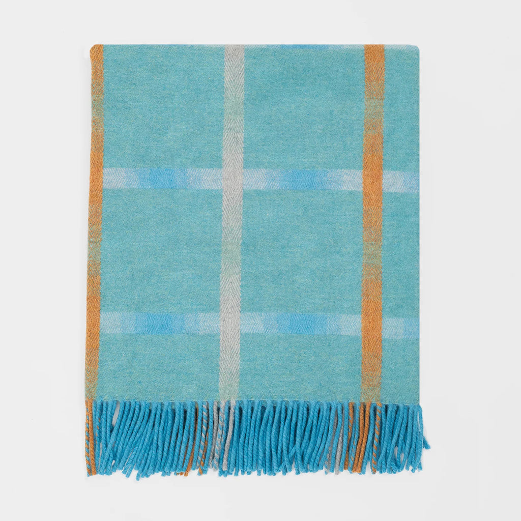 A folded plaid merino throw blanket with a light blue and turquoise base, featuring stripes in orange and subtle blue and cream. The bottom edge has matching fringed tassels.
