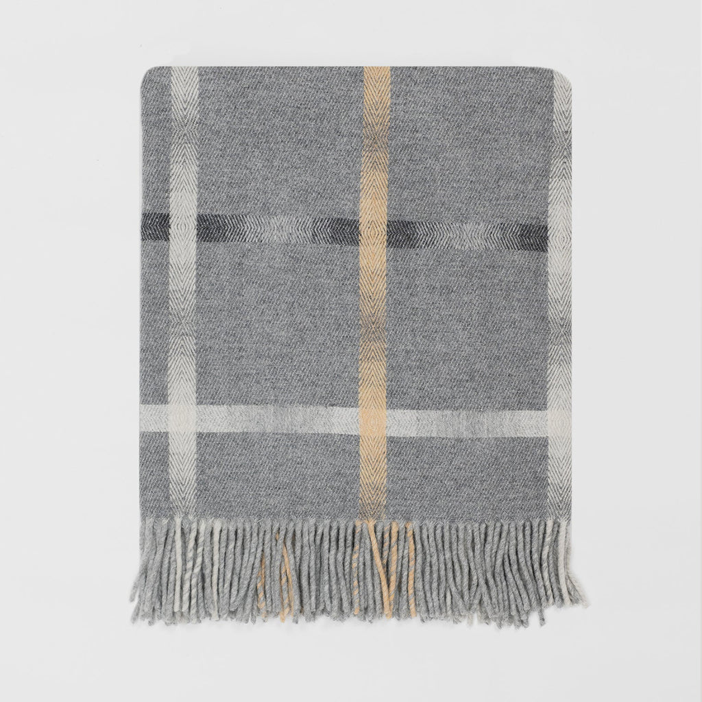 A grey lambswool merino plaid throw blanket with a vertical tan stripe and grey horizotonal stripe with fringed edges, displayed flat against a light grey background.