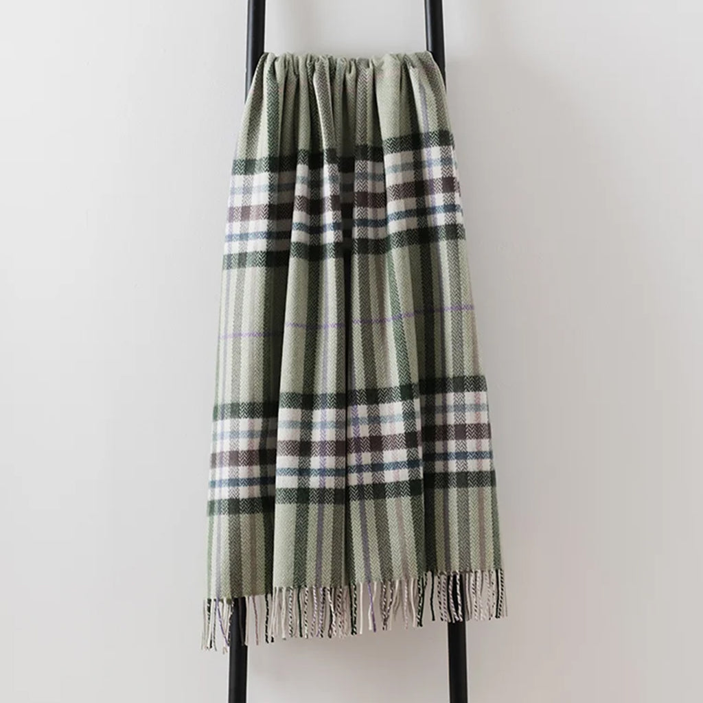 A 100% merino lambswool Remony throw draped over a black metal stand - in a jade green with brown overcheck  with an elegant fringe edge.