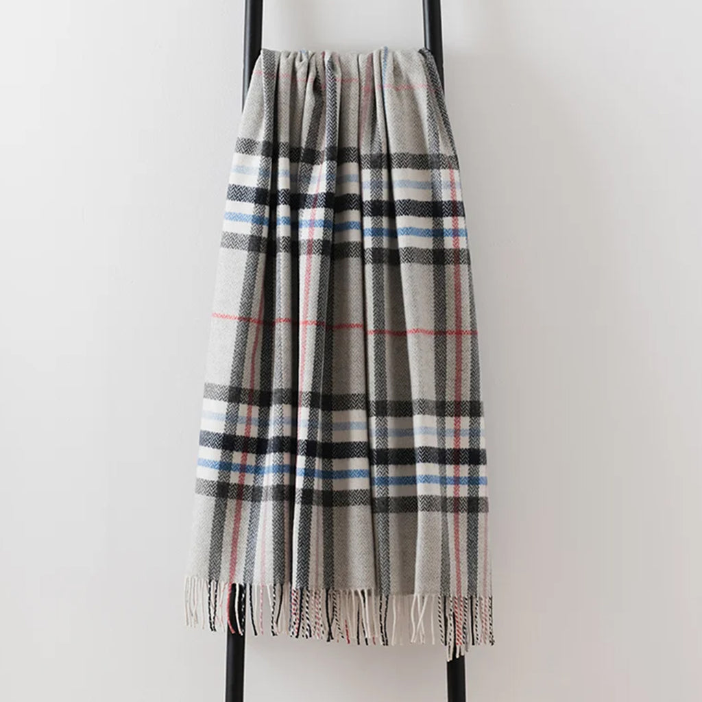A grey pewter tartan plaid throw with black, white, blue, and red stripes, draped over a black metal stand against a plain white wall.