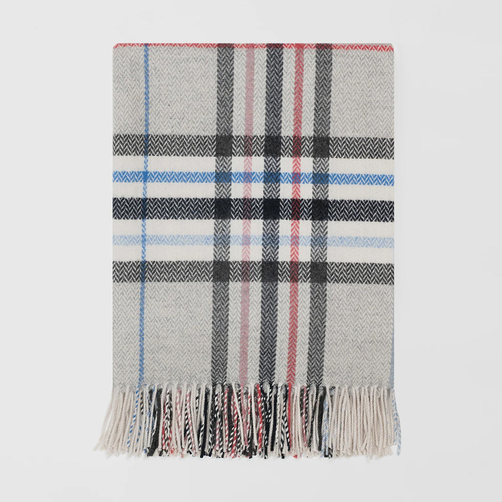 A classic plaid woven throw with fringe, featuring a light grey and white herringbone base with black, red, and blue stripes.