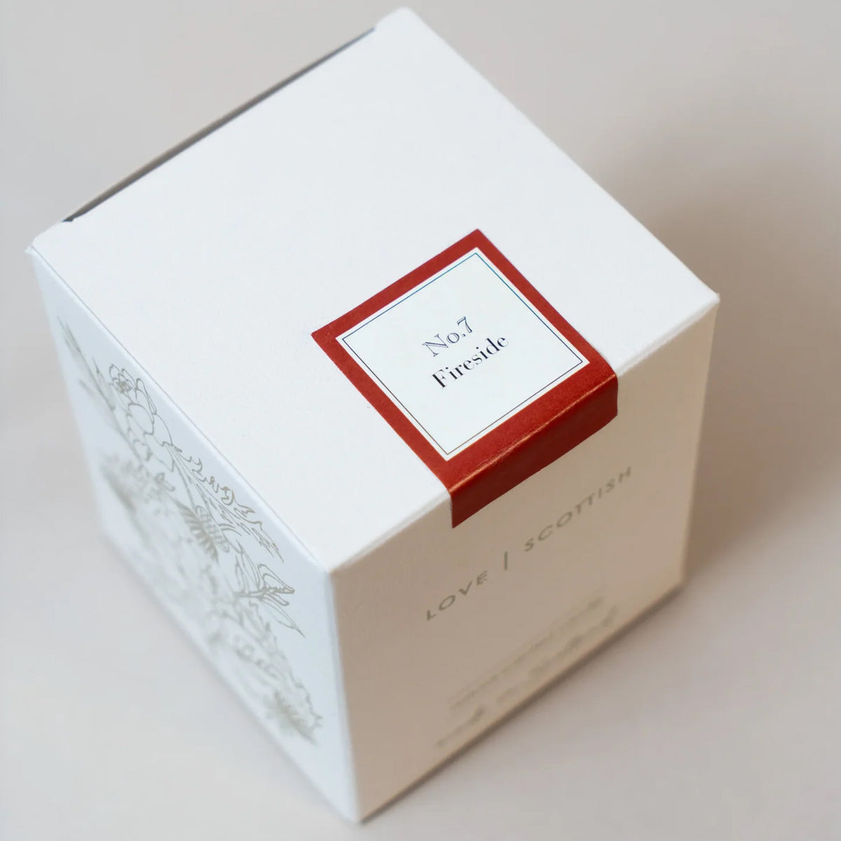 A white square product box with a red-bordered label reading 'No.17 Fireside Candle' and 'LOVE SCOTTISH' printed on the side, photographed on a light beige background.
