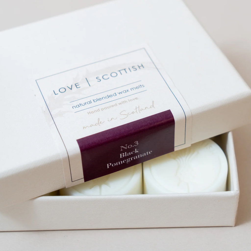A boxed set of wax melts with the lid partially open, showing two round off-white wax melts inside. The label reads 'LOVE SCOTTISH' scent Black Pomegranate No.3