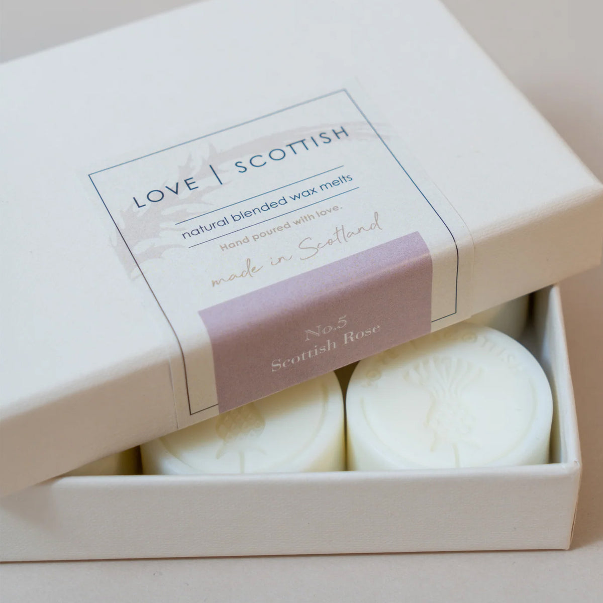 A boxed set of wax melts with the lid partially open, showing two round off-white wax melts inside. The label reads 'LOVE SCOTTISH' scent Scottish Rose No.5.