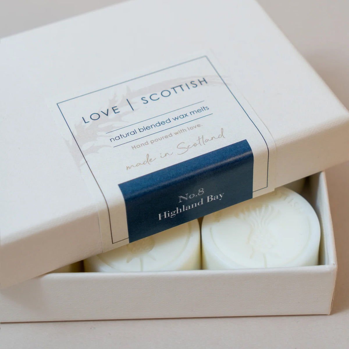 A white gift box containing two round white wax melts, with the lid partly lifted to reveal a label that reads 'LOVE | SCOTTISH' Scent Highland Bay, No.8