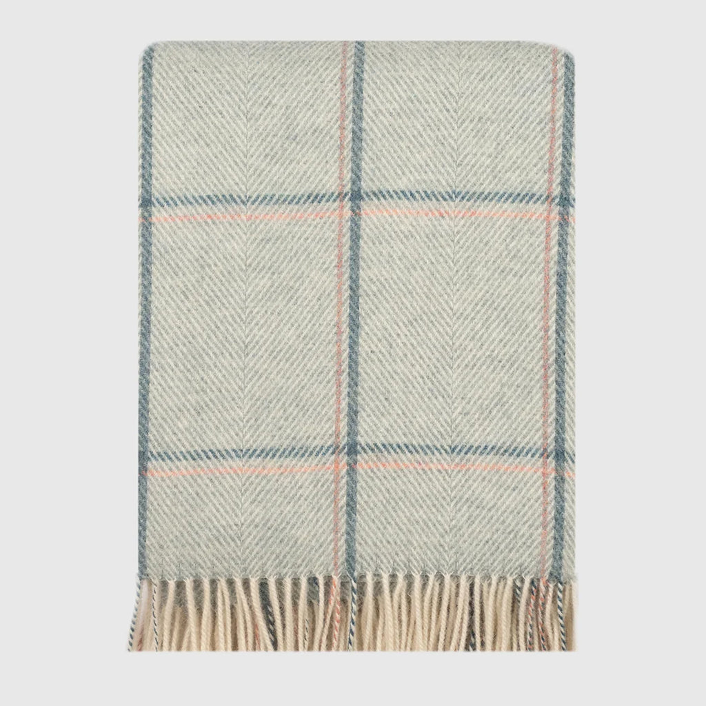 A folded woven throw blanket with a herringbone pattern in green hue, featuring a subtle plaid design with thin blue and pink lines, finished with fringed edges.