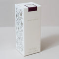 A tall white rectangular product box with botanical line drawings on the side, the words 'LOVE SCOTTISH' on the front, and a dark purple band near the top, inside a reed diffuser, pomegranate scent. photographed on a light neutral background.