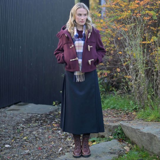 A women wearing boots and a burgundy coat and dress, with a classic tartan print lambswool scarf. 